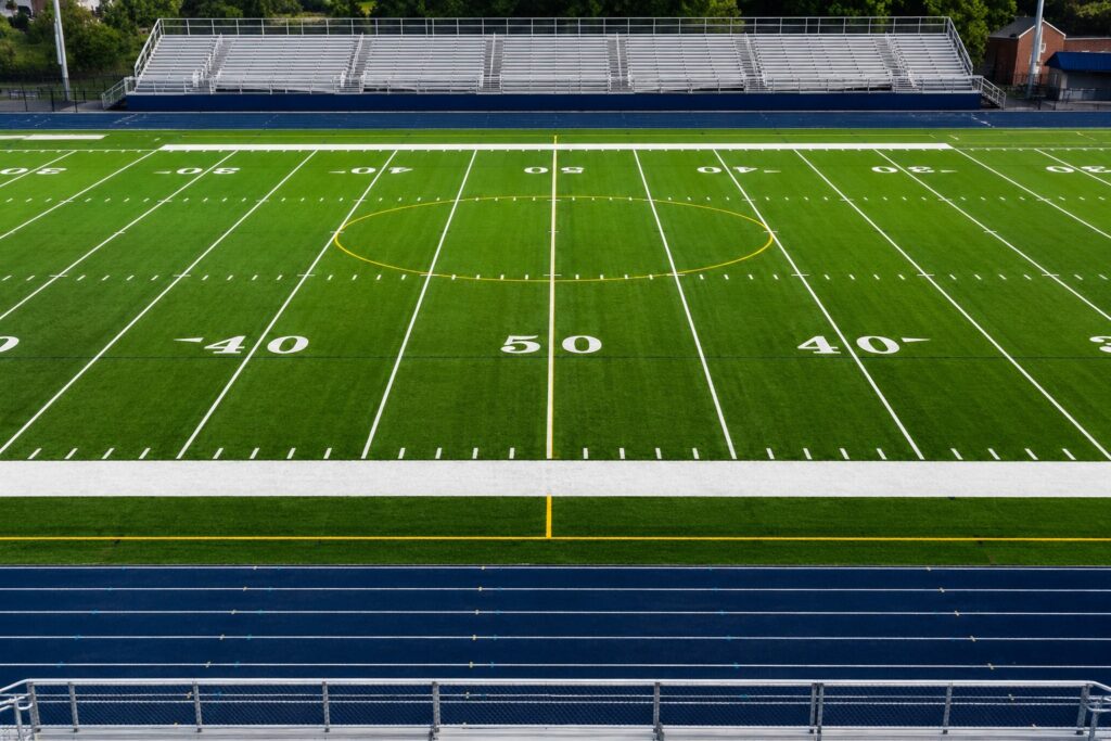Synthetic turf football field at a high school stadium with track and bleachers