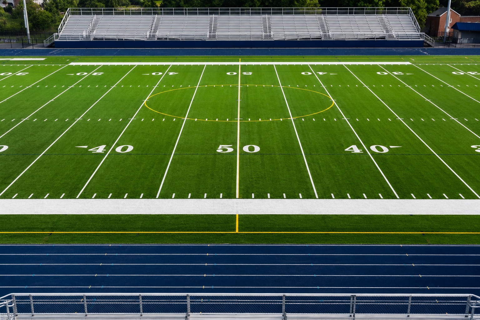 Synthetic turf football field at a high school stadium with track and bleachers